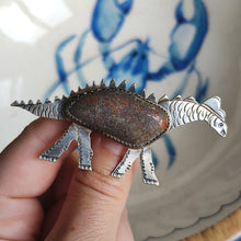 Load image into Gallery viewer, A silver long-necked dinosaur brooch with a hardstone body, held in a hand