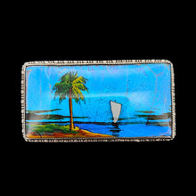 Load image into Gallery viewer, A butterfly wing brooch depicting a sailboat with a palm tree in the foreground, set in silver, on a black background