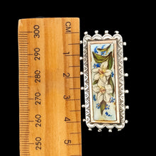 Load image into Gallery viewer, An oblong silver hobnail bead border brooch with an enamelled central plaque displaying flowers, next to a ruler