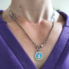 Load image into Gallery viewer, A hexagonal silver Saint Christopher pendant with blue and green enamel, attached to a silver chain and modelled by a woman wearing a purple top