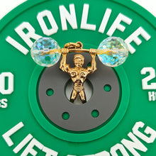 Load image into Gallery viewer, A yellow gold weightlifter charm pendant with a crystal barbell, in a green rubber power plate