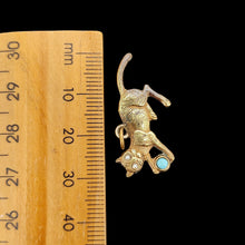Load image into Gallery viewer, A yellow metal cat playing with a blue ball charm, next to a ruler, on a black background