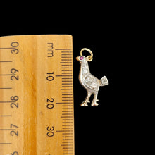 Load image into Gallery viewer, A diamond set bird charm in silver and yellow gold, with a ruby eye, next to a ruler on a black background