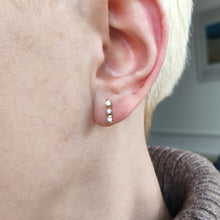 Load image into Gallery viewer, A yellow gold three stone diamond bar set stud earring, modelled in an ear