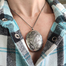 Load image into Gallery viewer, A silver oval locket with flower details, modelled with a silver chain