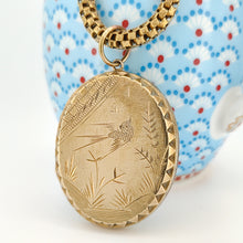 Load image into Gallery viewer, An oval locket with bird engraving with a Venetian link chain in yellow metal, sitting against a blue and white patterned jug