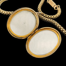 Load image into Gallery viewer, An oval locket, open, with a Venetian link chain in yellow metal, on a black background