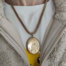 Load image into Gallery viewer, An oval locket with bird engraving with a Venetian link chain in yellow metal, modelled by a woman wearing a Pikachu t-shirt and fluffy jacket