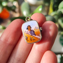 Load image into Gallery viewer, Small pendant with an Egyptian desert scene held between fingers against a blurred natural background