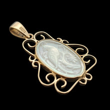 Load image into Gallery viewer, An oval yellow gold and mother of pearl pendant carved with a bird, on a black background