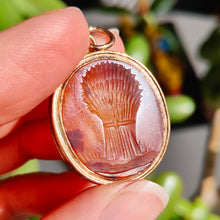 Load image into Gallery viewer, An oval carnelian intaglio pendant displaying a wheatsheaf, held in a hand
