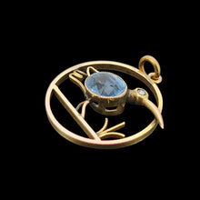 Load image into Gallery viewer, A circular cutout pendant featuring a wading bird with a blue paste stone body, in yellow gold, on a black background
