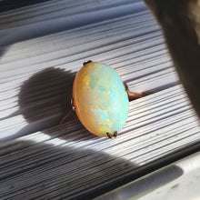 Load image into Gallery viewer, A single stone oval shaped, cabochon cut opal ring in rose gold, in the pages of a book