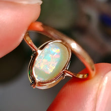 Load image into Gallery viewer, A single stone oval shaped, cabochon cut opal ring in rose gold, held in a hand