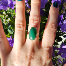 Load image into Gallery viewer, An oval nephrite jade ring in white and yellow gold, modelled on a hand, with purple flowers in the background