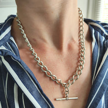 Load image into Gallery viewer, A silver curb link Albert chain with lobster clasp and T-bar, modelled by a woman wearing a stripey shirt
