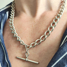 Load image into Gallery viewer, A silver curb link Albert chain with lobster clasp and T-bar, modelled by a woman wearing a stripey shirt
