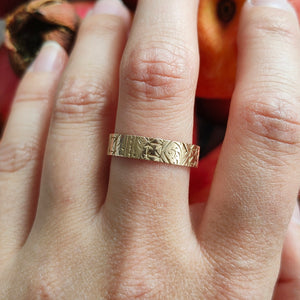Gold ring with intricate design on a finger against a blurred background