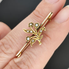 Load image into Gallery viewer, A yellow gold floral bar brooch with seed pearls, held between fingers
