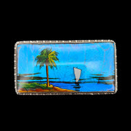 A butterfly wing brooch depicting a sailboat with a palm tree in the foreground, set in silver, on a black background