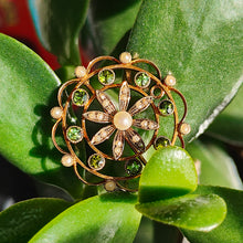 Load image into Gallery viewer, A circular brooch/pendant in yellow gold with peridots and pearls, with a flower to the centre, on leaves
