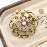 A circular brooch/pendant in yellow gold with peridots and pearls, with a flower to the centre, in an antique box