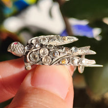 Load image into Gallery viewer, An antique swallow bird brooch in silver with paste stones, held in a hand
