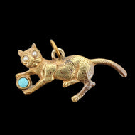 A yellow metal cat playing with a blue ball charm, on a black background