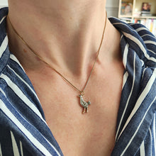 Load image into Gallery viewer, A diamond set bird charm in silver and yellow gold, with a ruby eye, with a chain and modelled by a woman wearing a stripey shirt

