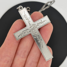 Load image into Gallery viewer, A silver cross pendant engraved with a bird and vines, with a curb link chain, held in a hand

