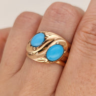 A rose gold double snake band ring with turquoise heads, modelled on a hand