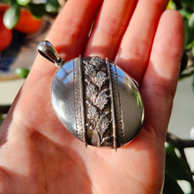 Load image into Gallery viewer, An oval silver locket pendant with acorn and oak leaf detailing held in a hand, with leaves in the background
