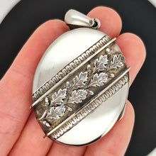 Load image into Gallery viewer, An oval silver locket pendant with acorn and oak leaf detailing held in a hand
