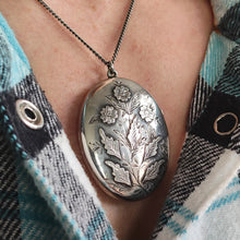 Load image into Gallery viewer, A silver oval locket with flower details, modelled with a silver chain
