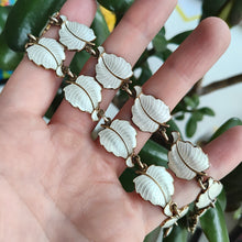 Load image into Gallery viewer, A white enamel leaf necklace in silver gilt, held in a hand
