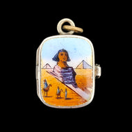An enamelled silver charm pendant depicting an Egyptian desert scene, on a black background