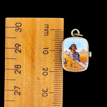 Load image into Gallery viewer, Small pendant with a design of a sphinx in a desert scene next to a wooden ruler for scale
