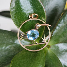 Load image into Gallery viewer, A circular cutout pendant featuring a wading bird with a blue paste stone body, in yellow gold, sitting on leaves

