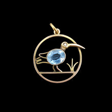 Load image into Gallery viewer, A circular cutout pendant featuring a wading bird with a blue paste stone body, in yellow gold, on a black background
