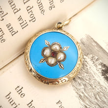 Load image into Gallery viewer, Victorian 9ct Gold Enamel, Pearl and Garnet Glazed Back Pendant sat on the open pages of a book
