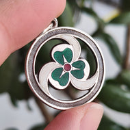 A silver enamel clover triskelion pendant, held in a hand