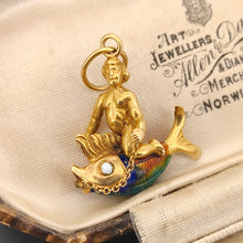 Load image into Gallery viewer, A gold pendant depicting a figure riding a fish, sat in an antique box. The fish has colourful enamel scales in blue, green, and orange. A gold chain connects the figure to the fish. The pendant has a small gold loop at the top for attaching to a chain.
