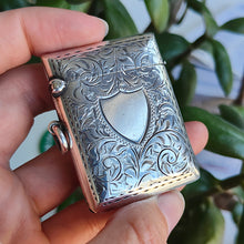 Load image into Gallery viewer, A silver rectangular engraved vesta case with a shield cartouche, held in a hand
